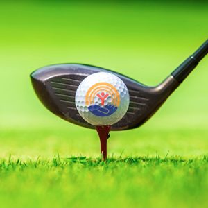 A golf club is behind a ball with the United Way logo in front of it.